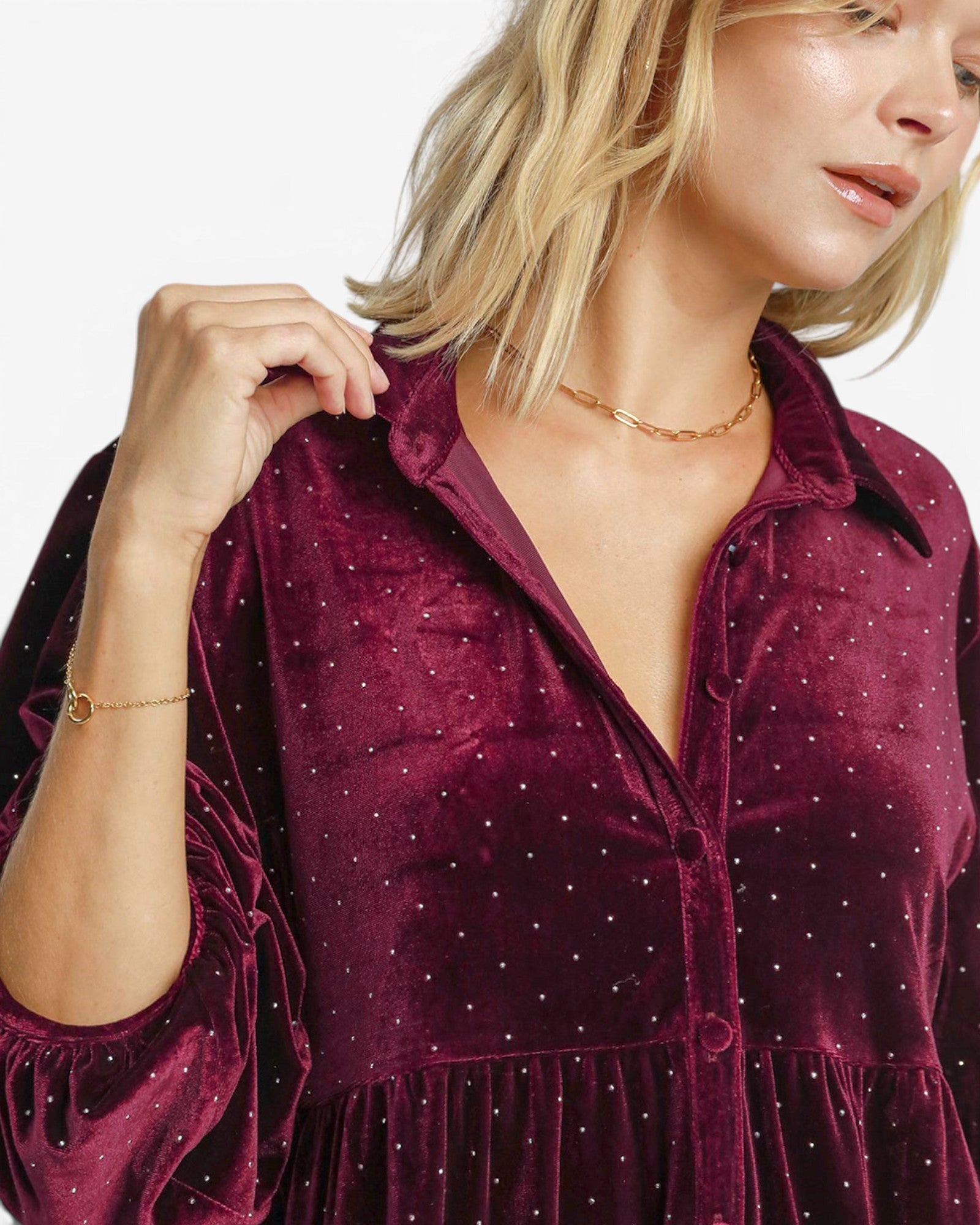 A close-up of a woman wearing a deep burgundy velvet button-up shirt dress with tiny silver rhinestone dots, set against a clean white background.