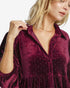 A close-up of a woman wearing a deep burgundy velvet button-up shirt dress with tiny silver rhinestone dots, set against a clean white background.