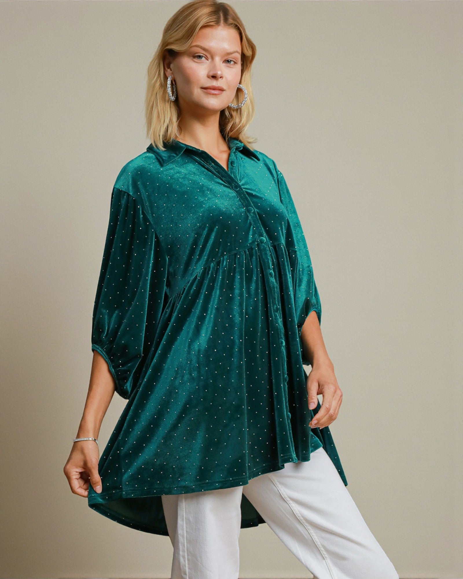 Woman wearing a green velvet tunic with white pants against a neutral background