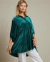 Woman wearing a green velvet tunic with white pants against a neutral background