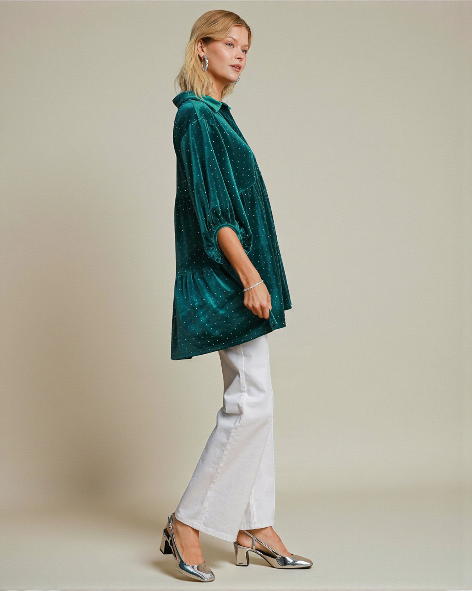 Woman wearing a green velvet shirt and white pants on a plain background