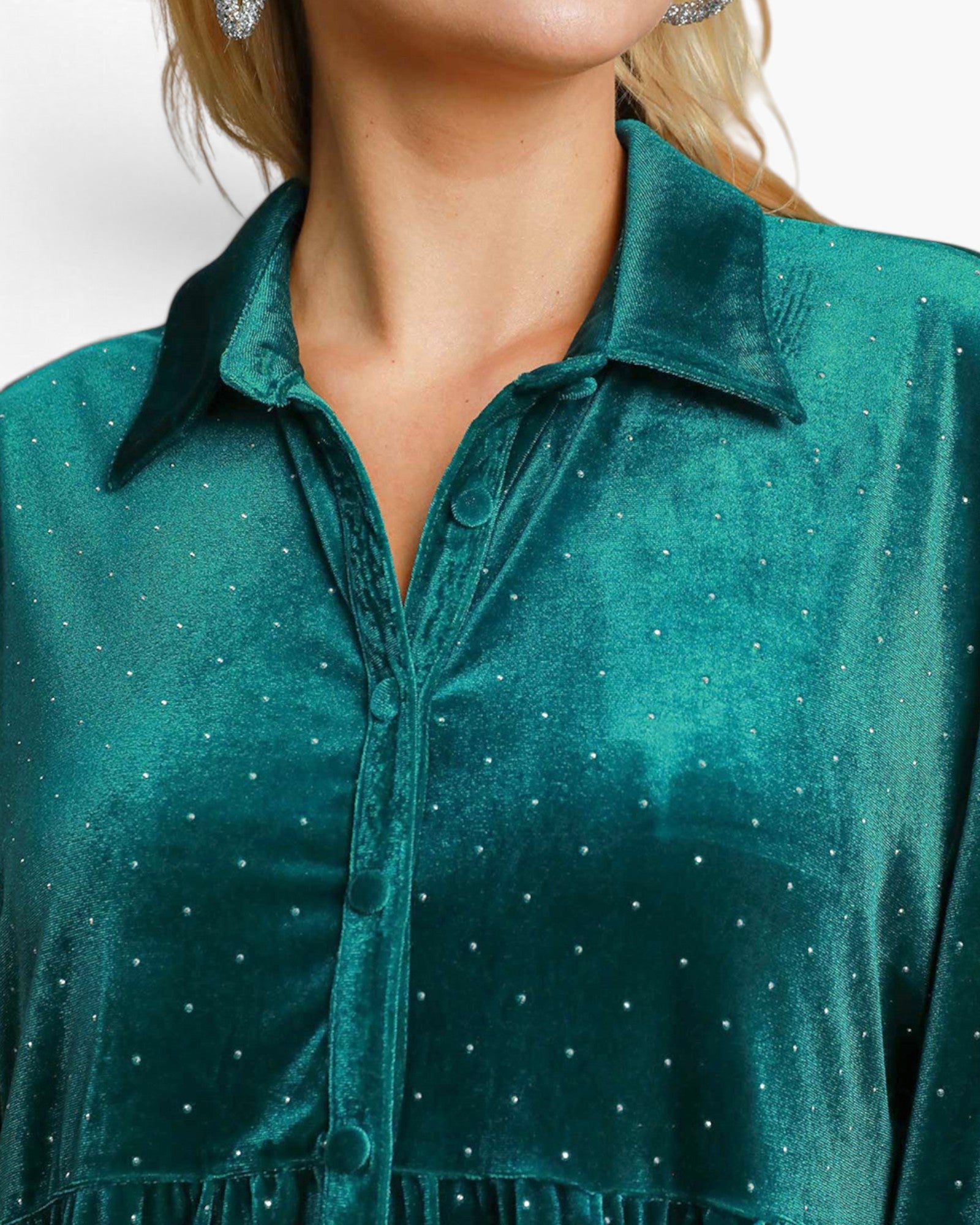 A close-up of a woman wearing a teal green velvet button-up shirt with small silver rhinestone embellishments, shown against a plain light background.
