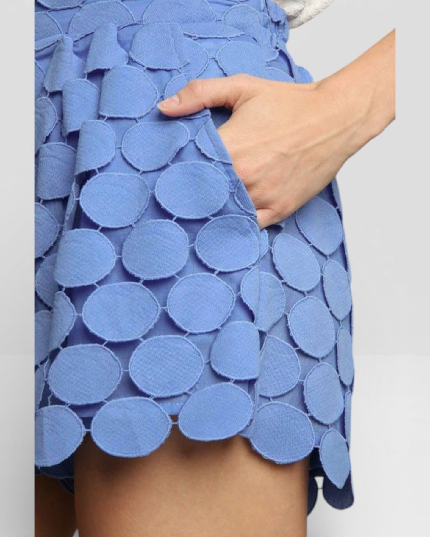Blue skirt with circular patterns held by a hand on a light gray background