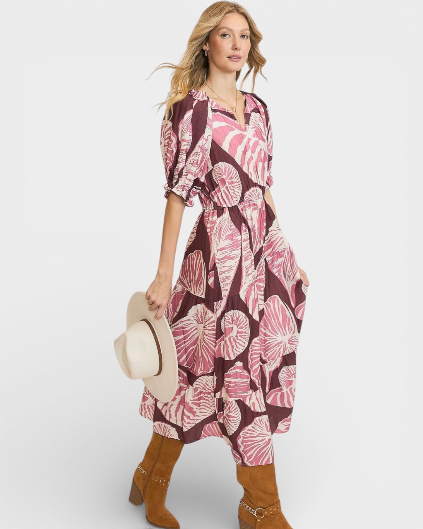 Woman wearing a pink and purple floral dress holding a hat on a white background