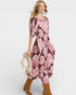 Woman wearing a pink and purple floral dress holding a hat on a white background