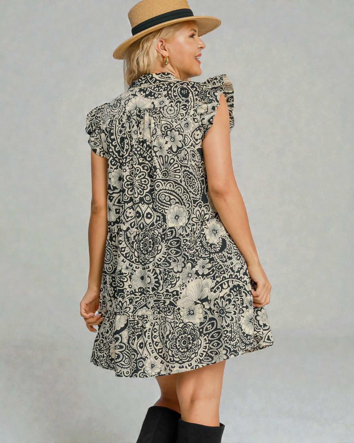 Woman wearing a patterned dress and hat on a plain background