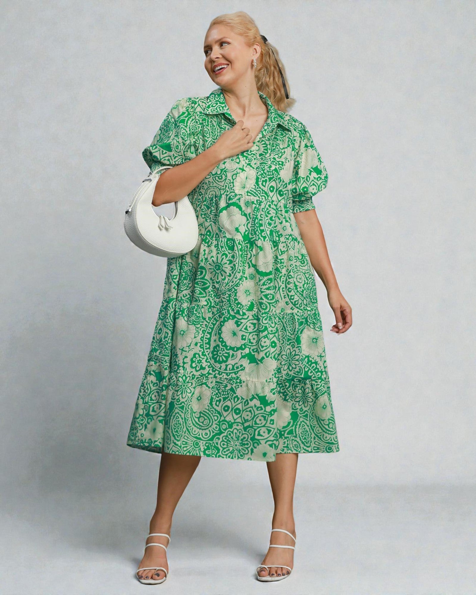 Woman wearing a green patterned dress holding a white handbag against a plain background