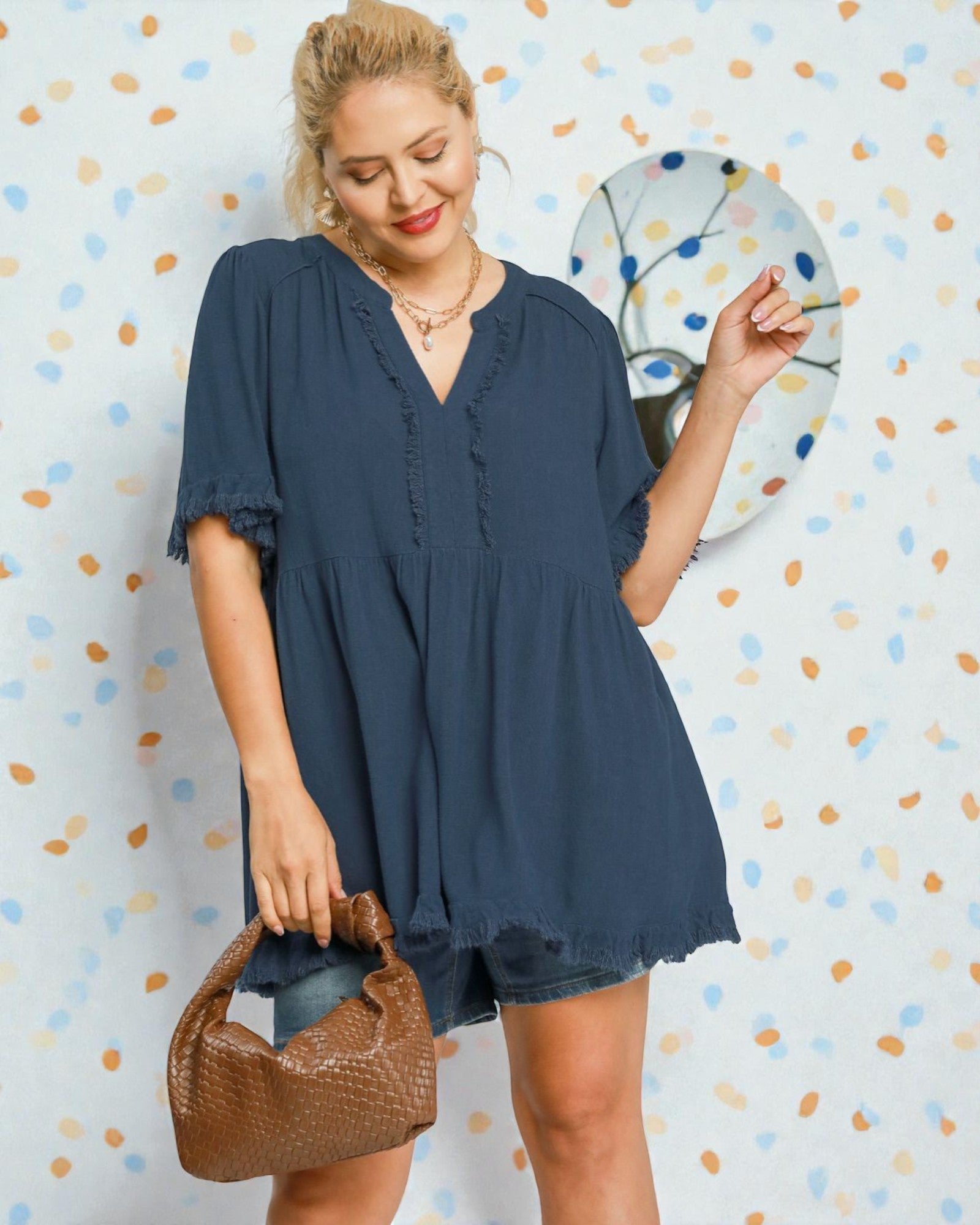 Woman wearing a blue dress holding a brown bag against a polka dot wall.