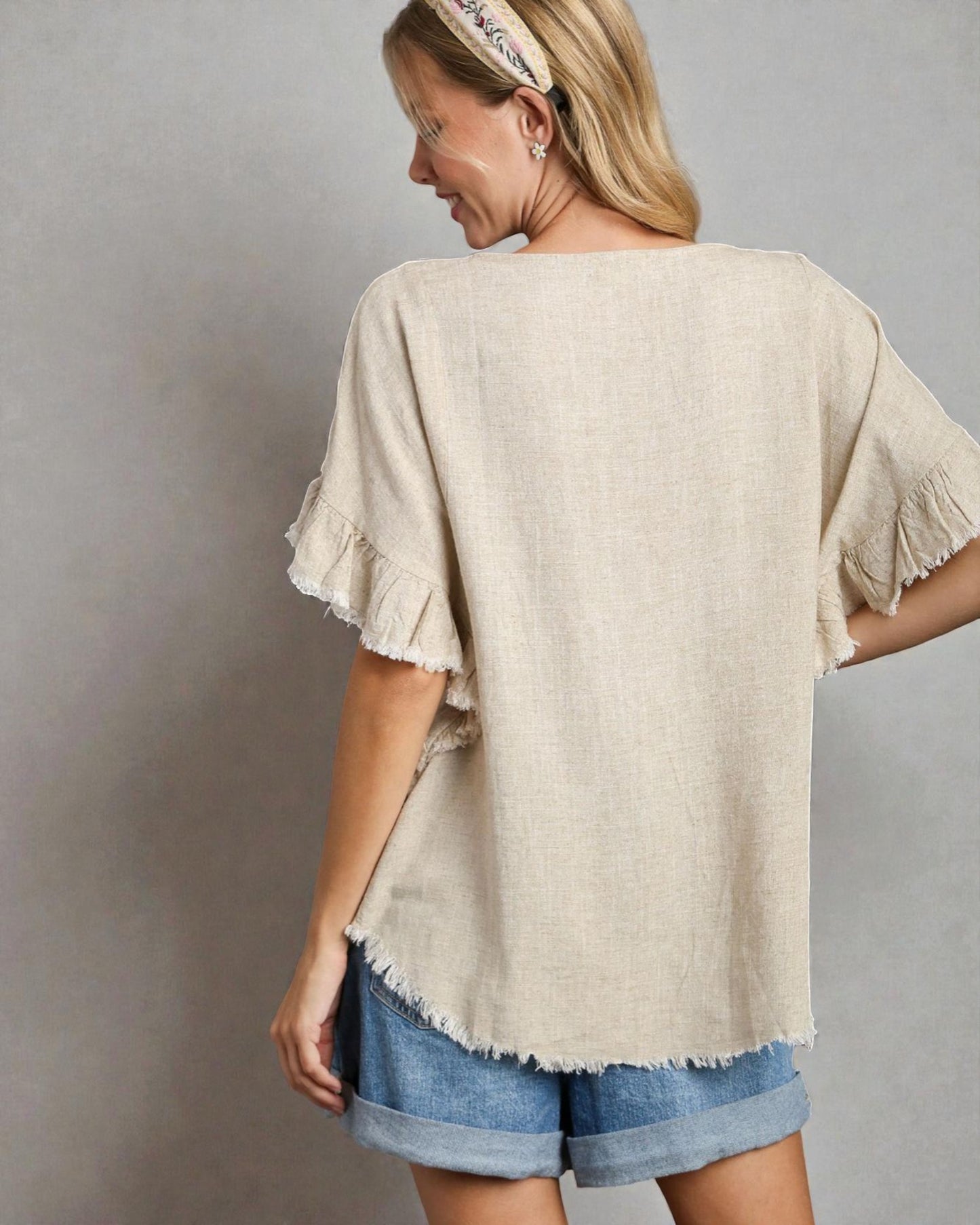 Woman wearing a beige ruffled top and denim shorts against a gray background