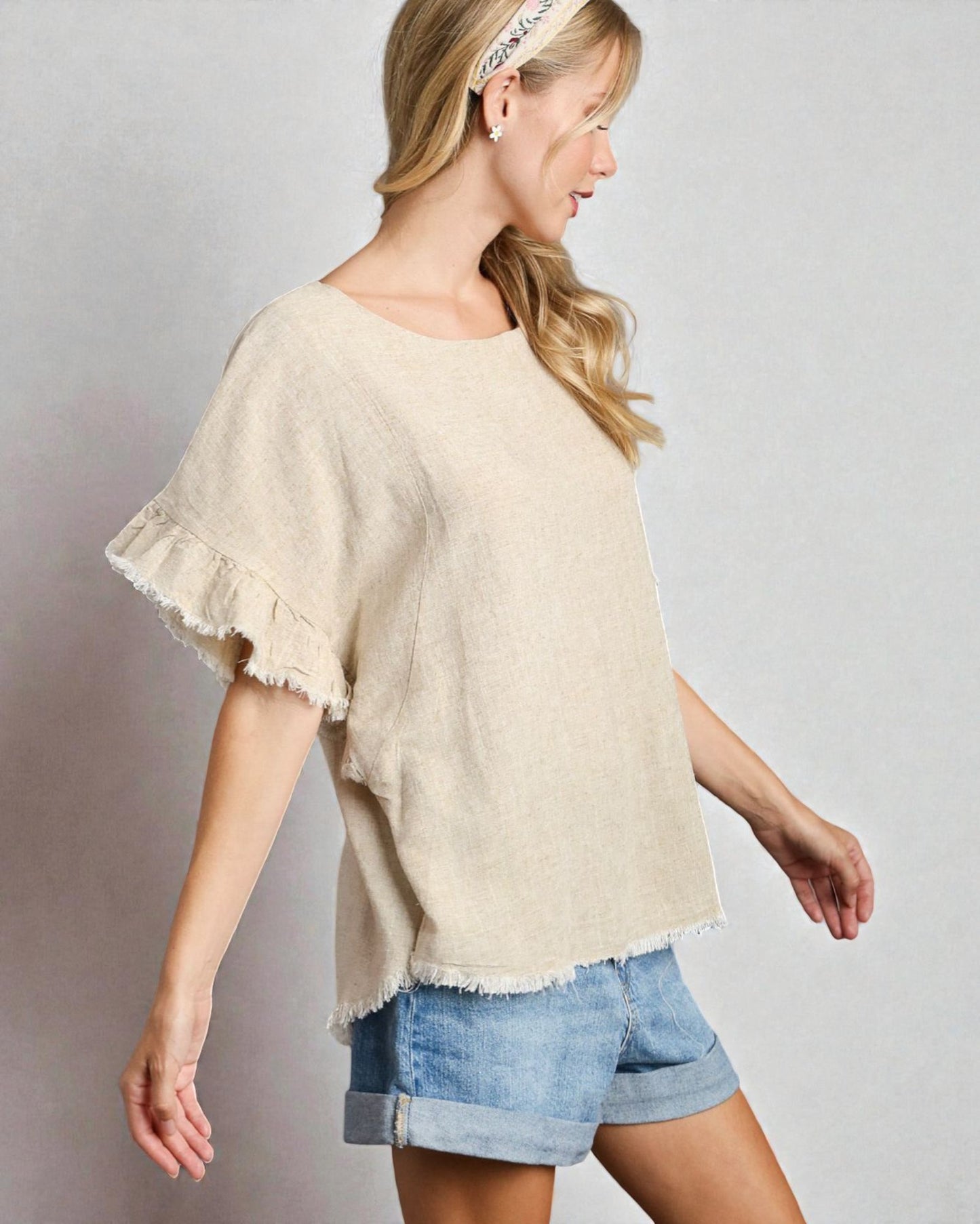 Woman wearing a beige top and denim shorts on a plain background