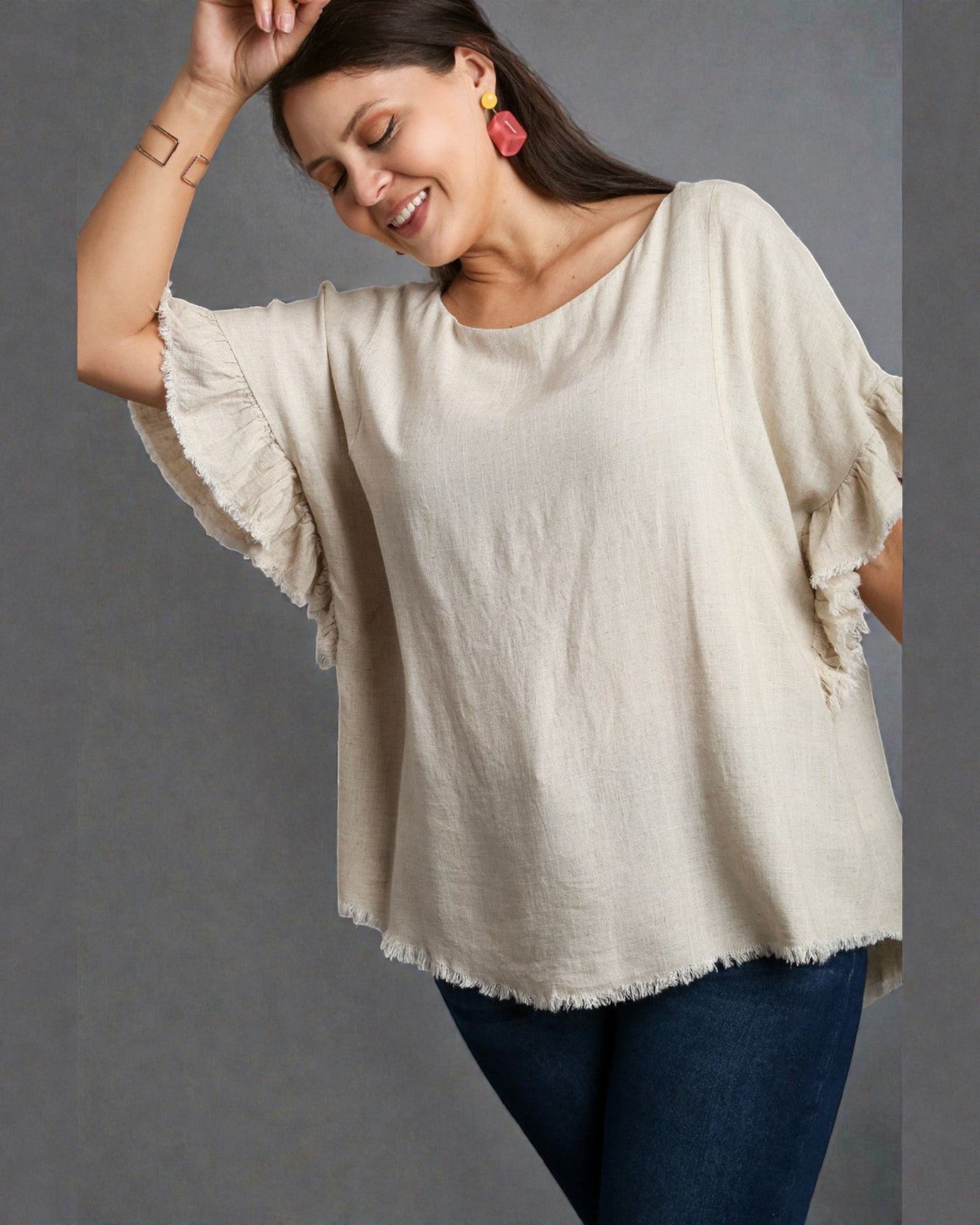 Woman wearing a beige top with ruffled sleeves against a gray background