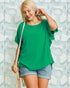Woman wearing a green top and denim shorts against a textured light blue wall.