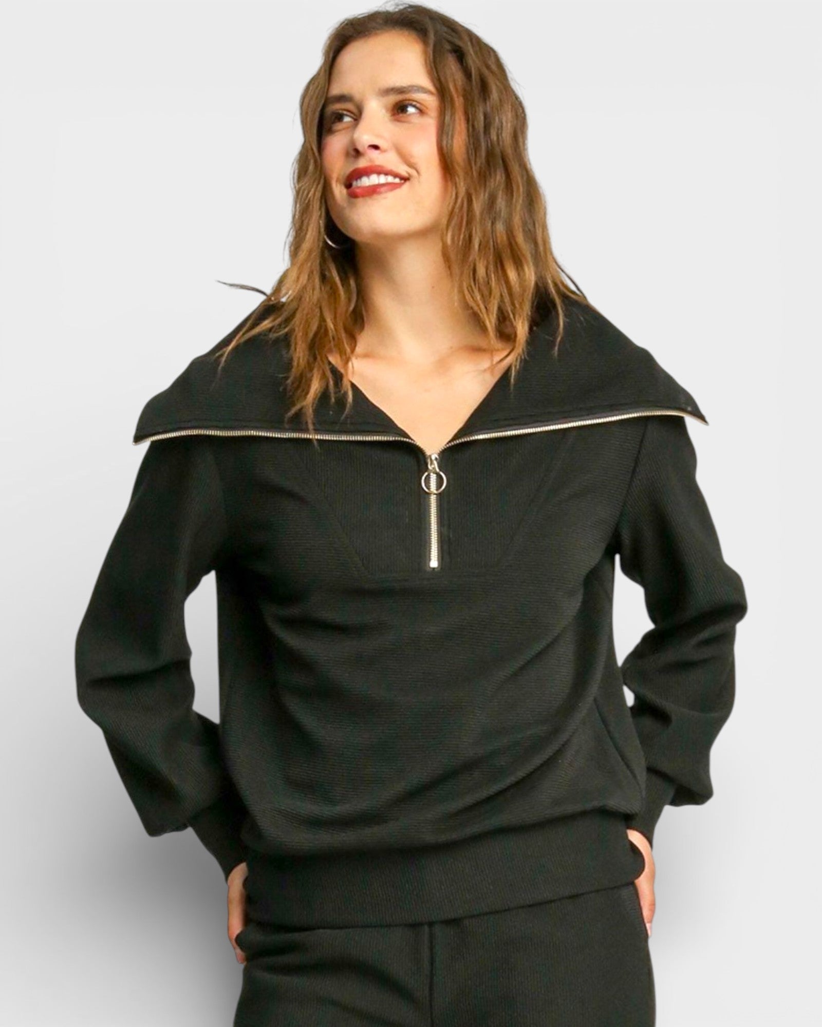 Woman wearing a black outfit with a zipper detail on a plain background