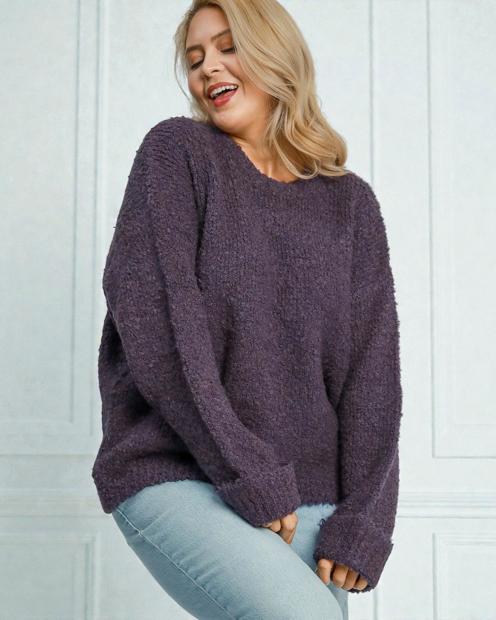 Woman wearing a purple sweater against a white paneled wall