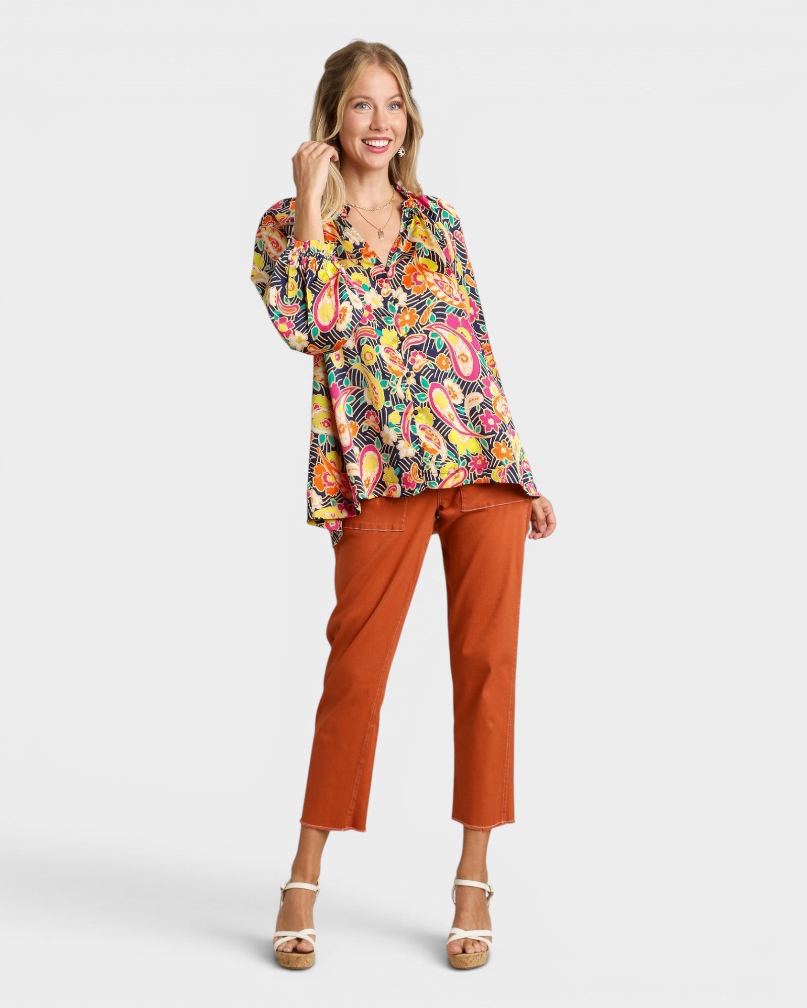 Woman wearing a colorful patterned blouse and orange pants on a white background