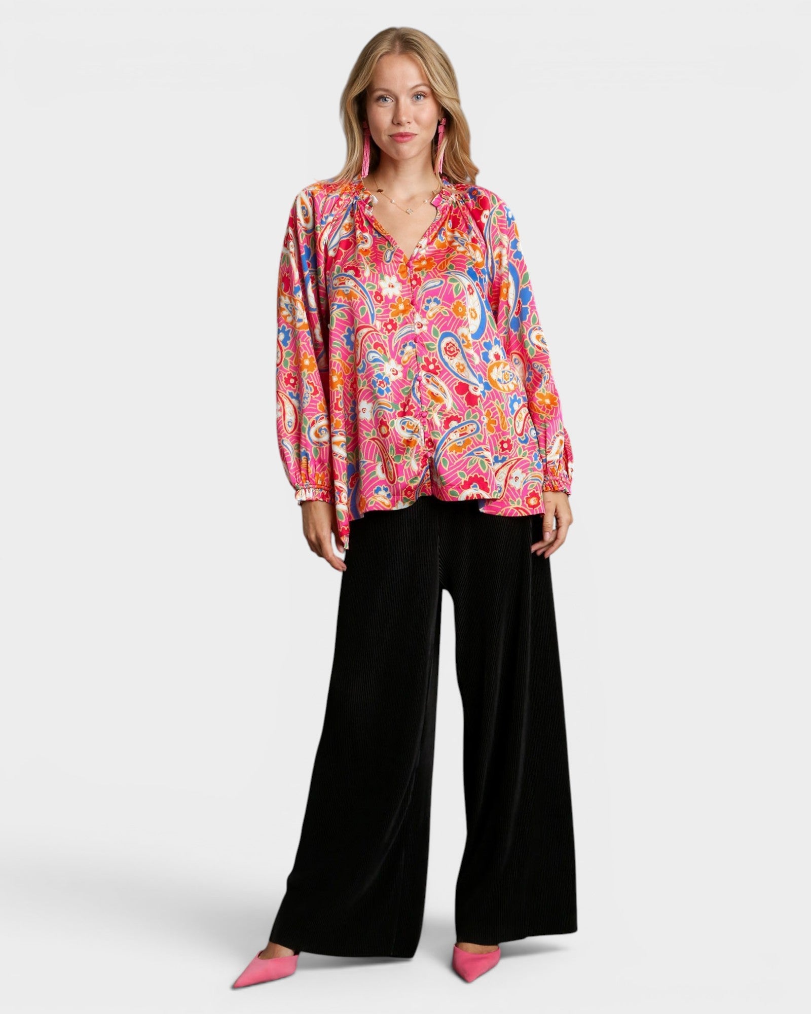 Woman wearing a colorful paisley blouse and black pants on a white background