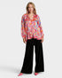 Woman wearing a colorful paisley blouse and black pants on a white background