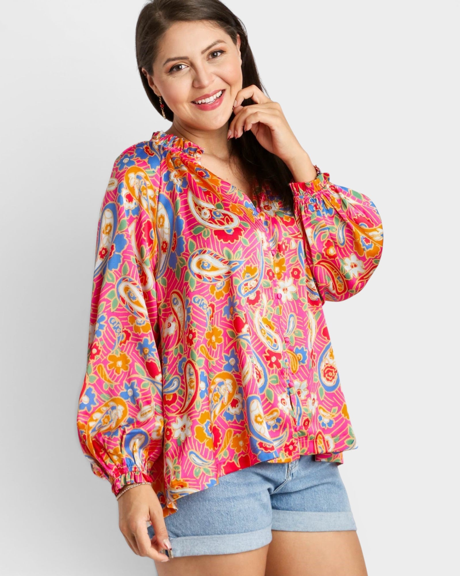 Woman wearing a colorful patterned blouse with denim shorts on a white background