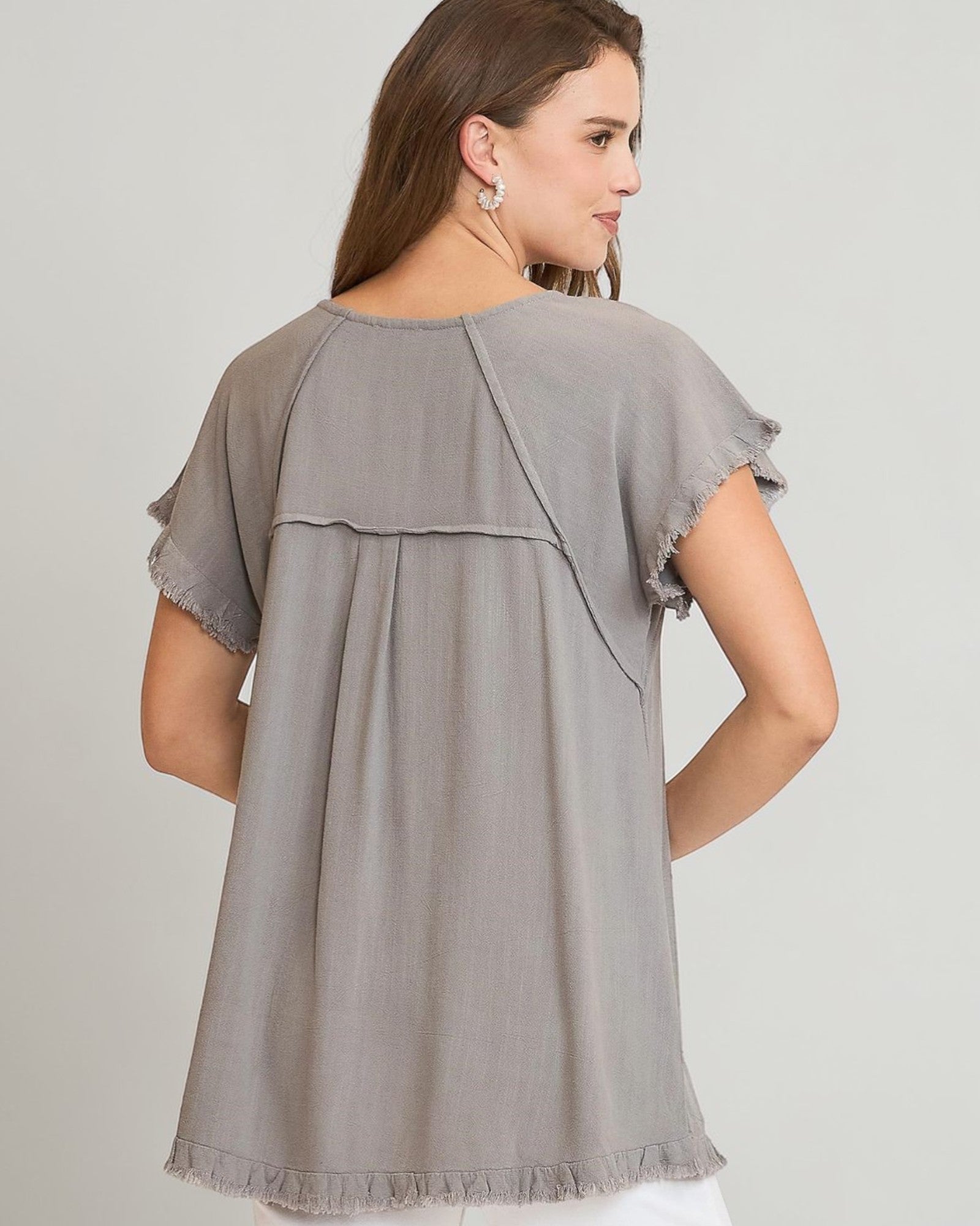 Woman wearing a gray blouse with ruffled sleeves on a plain background
