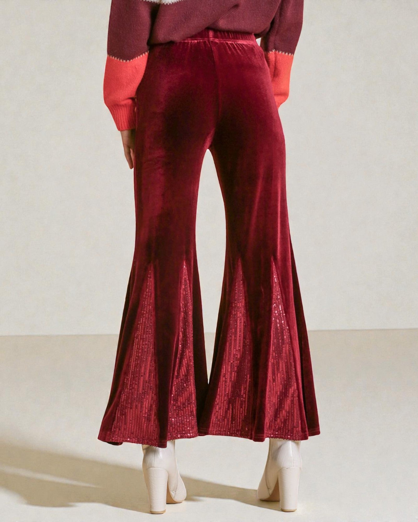 Red velvet flared pants worn by a person on a plain background