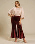 Woman wearing a light pink blouse and burgundy velvet pants against a beige background