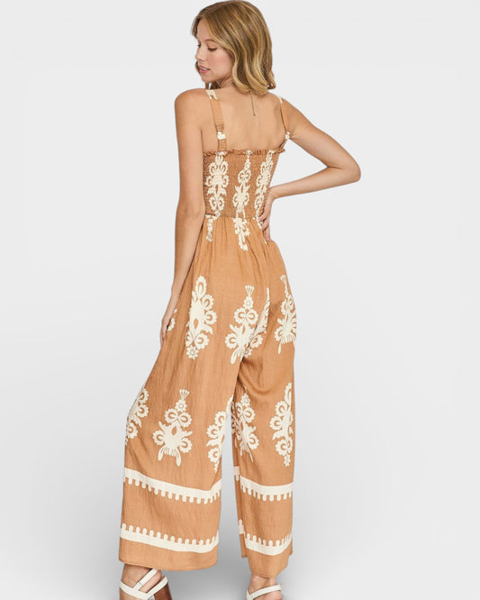 Woman wearing a tan jumpsuit with white lace patterns on a light gray background