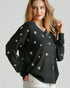 Woman wearing a black sweater with star patterns on a plain background