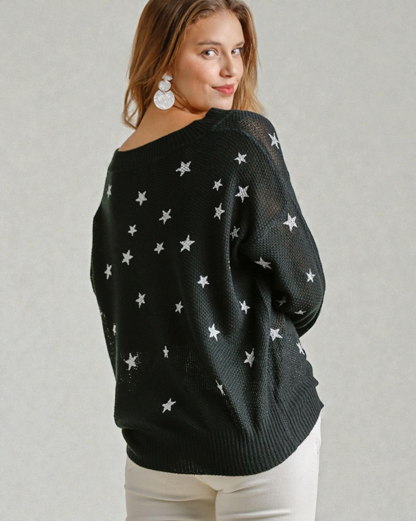 Woman wearing a black sweater with star patterns on a plain background
