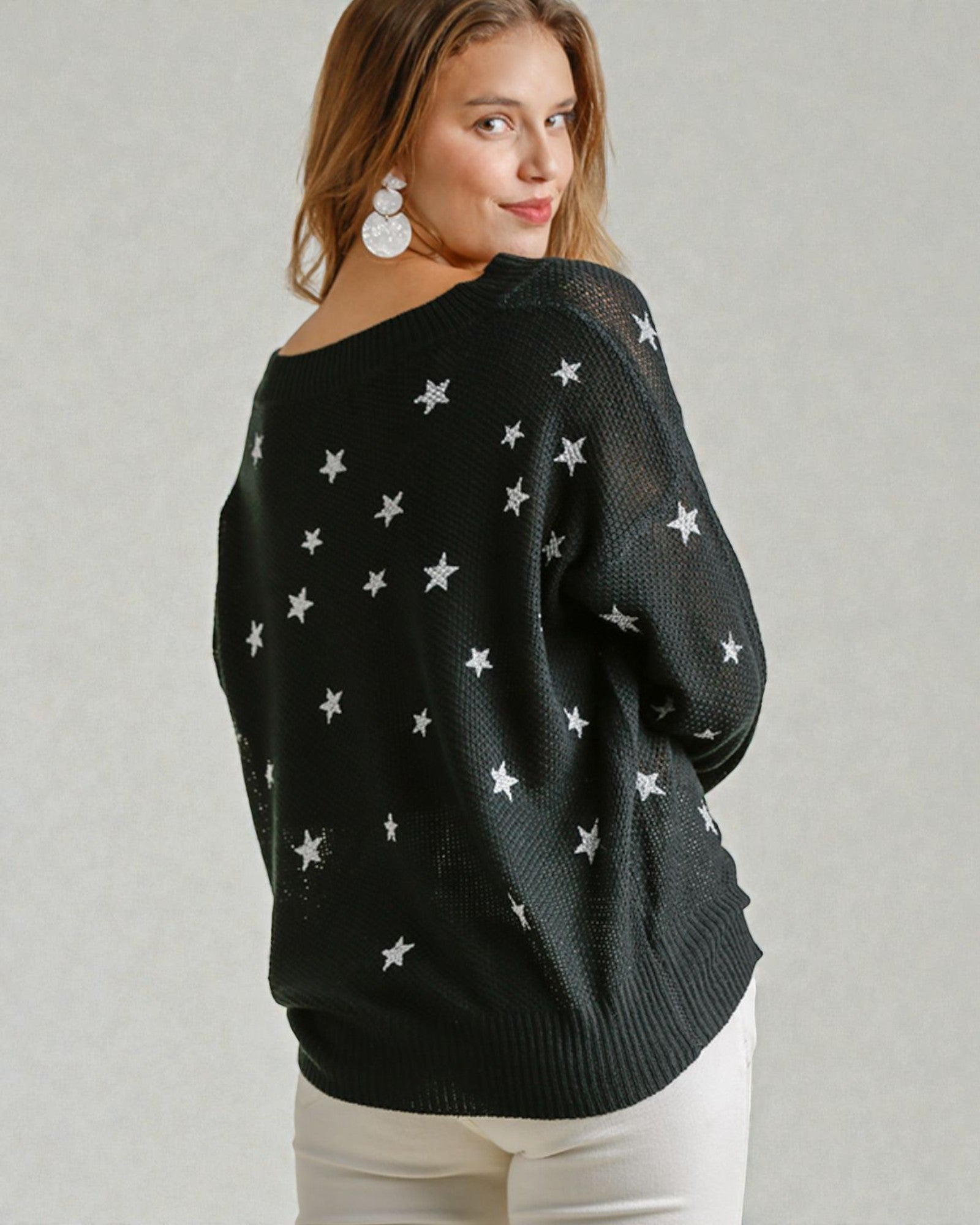 Woman wearing a black sweater with star patterns on a plain background