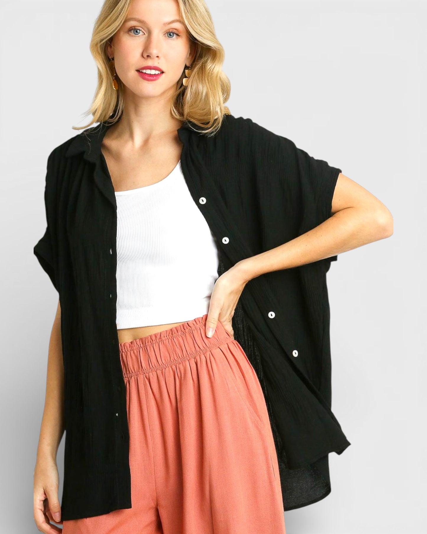 Woman wearing a black sleeveless jacket over a white top and pink pants on a light gray background