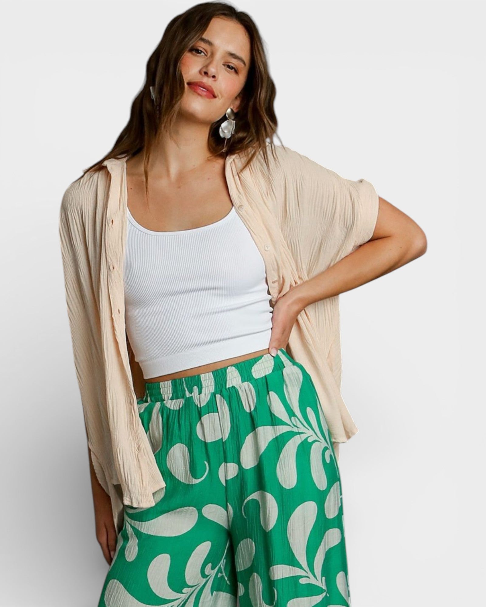 Woman wearing a white top and green patterned pants with a beige cardigan on a white background