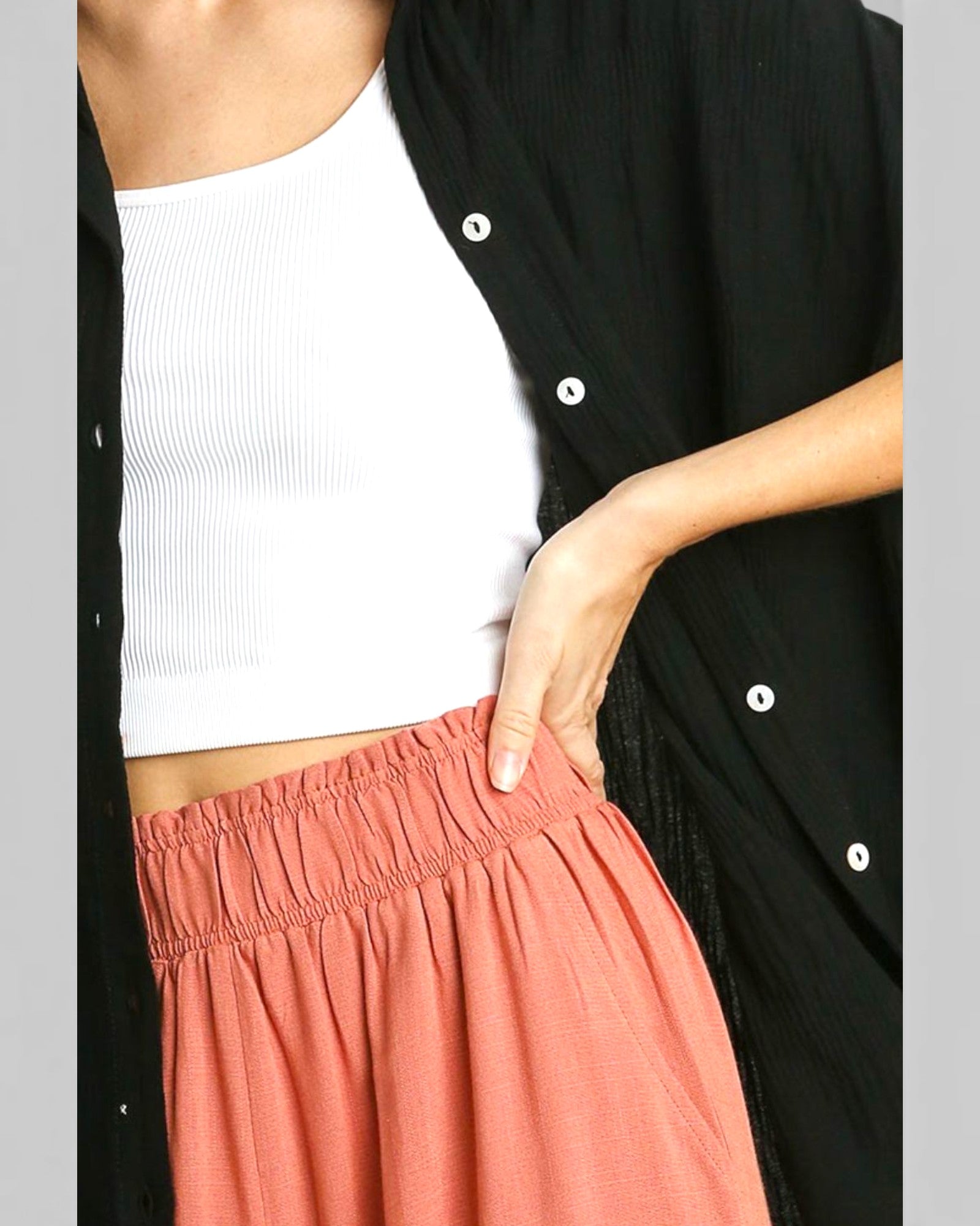 Person wearing a black cardigan, white top, and pink pants on a gray background