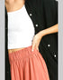 Person wearing a black cardigan, white top, and pink pants on a gray background
