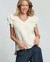 Woman wearing a white textured top with ruffled sleeves and blue jeans on a light gray background