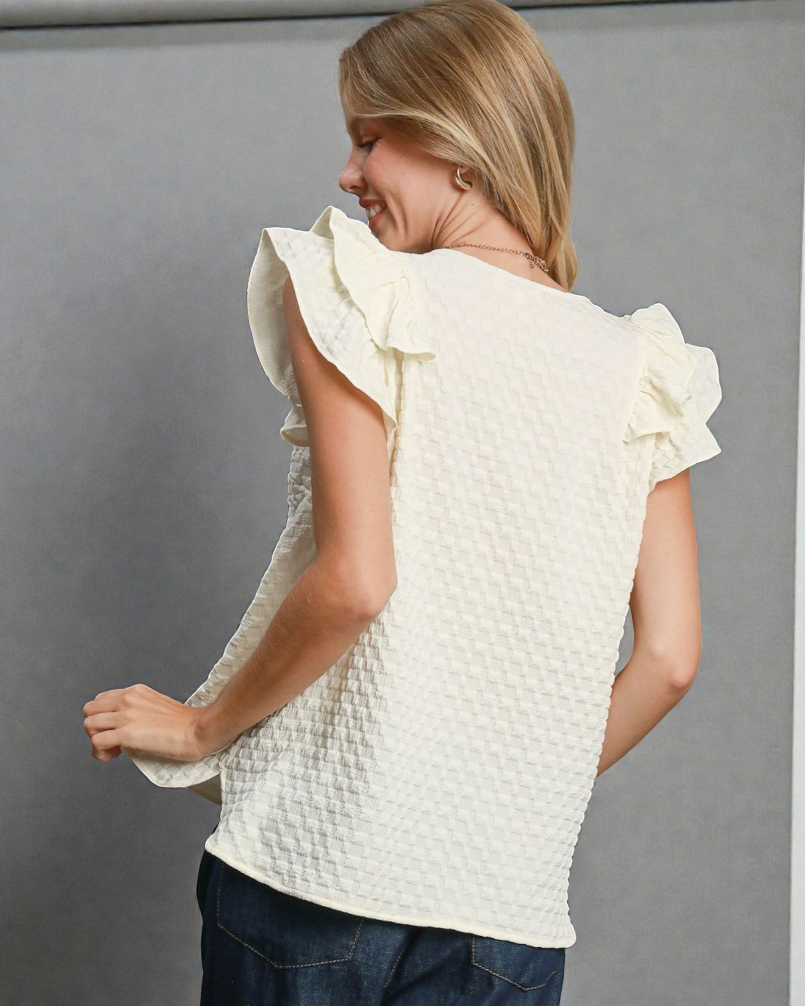 Woman wearing a white textured top with ruffled sleeves against a gray background