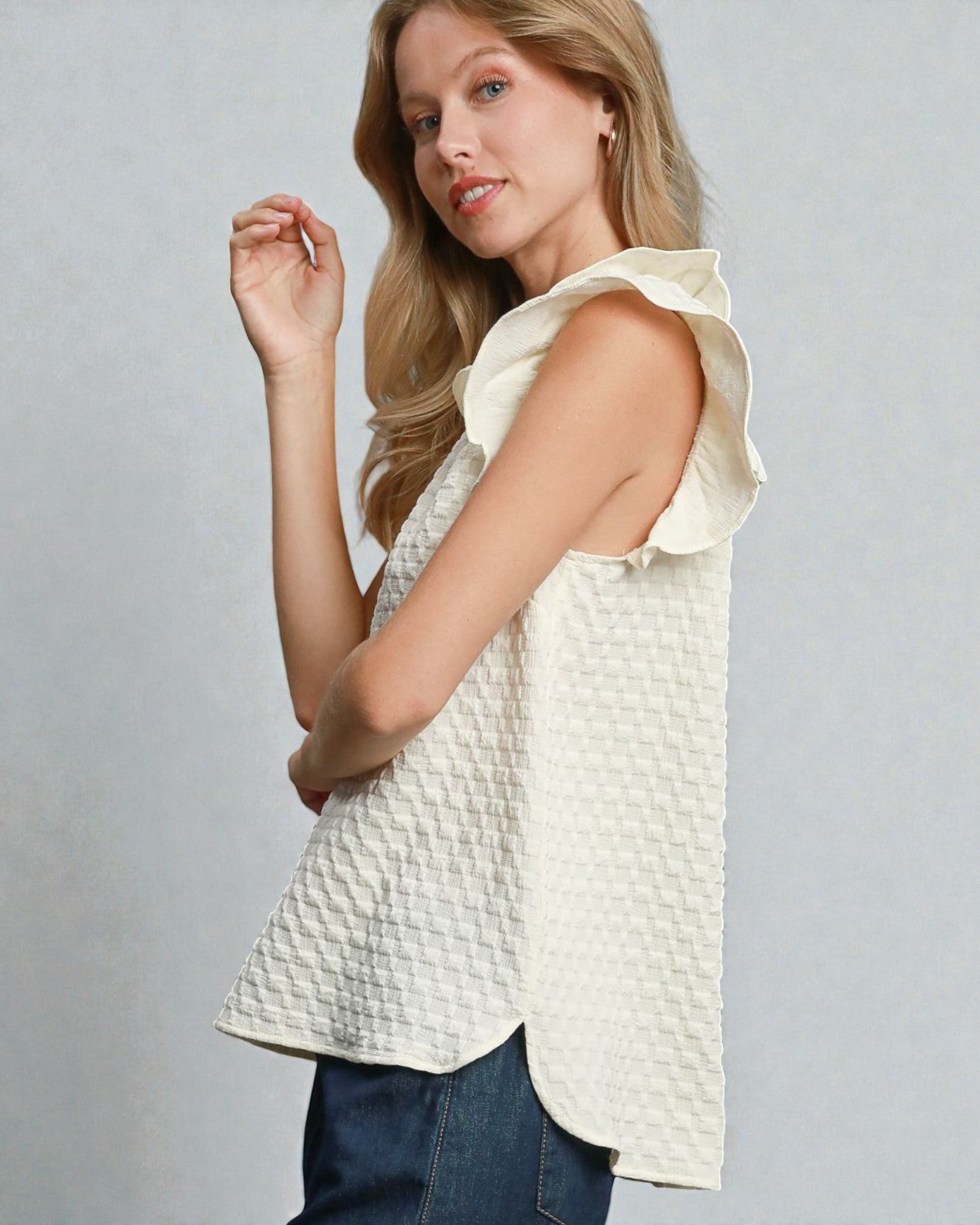Woman wearing a light-colored blouse with ruffled sleeves on a gray background