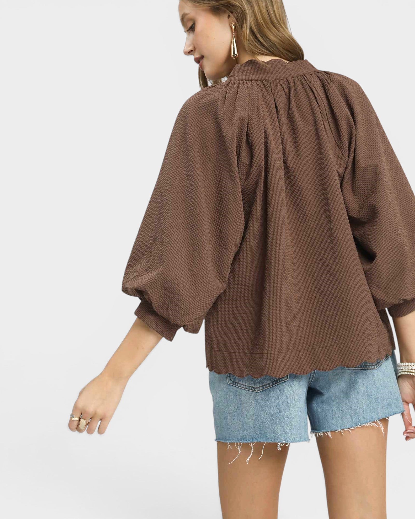 Woman wearing a brown blouse and denim shorts on a white background
