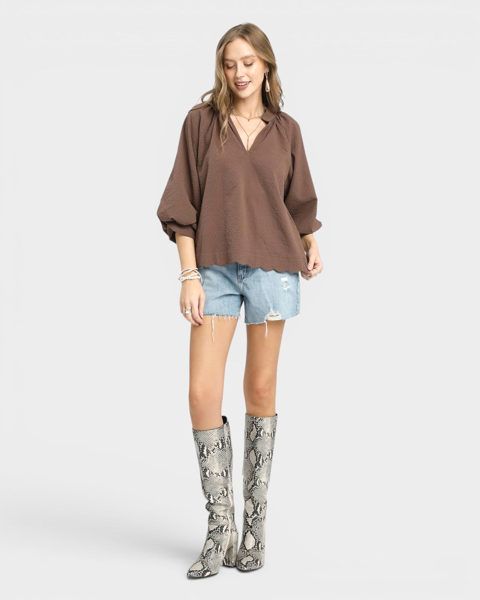Woman wearing a brown blouse, light blue shorts, and patterned knee-high boots on a white background