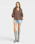 Woman wearing a brown blouse, light blue shorts, and patterned knee-high boots on a white background