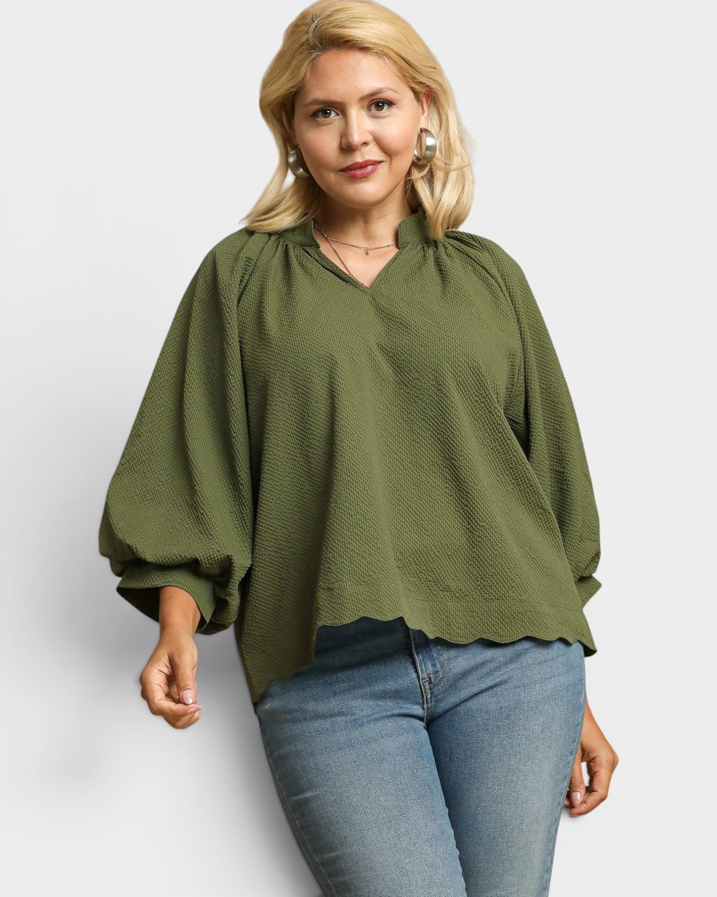 Woman wearing an olive green blouse and blue jeans on a white background