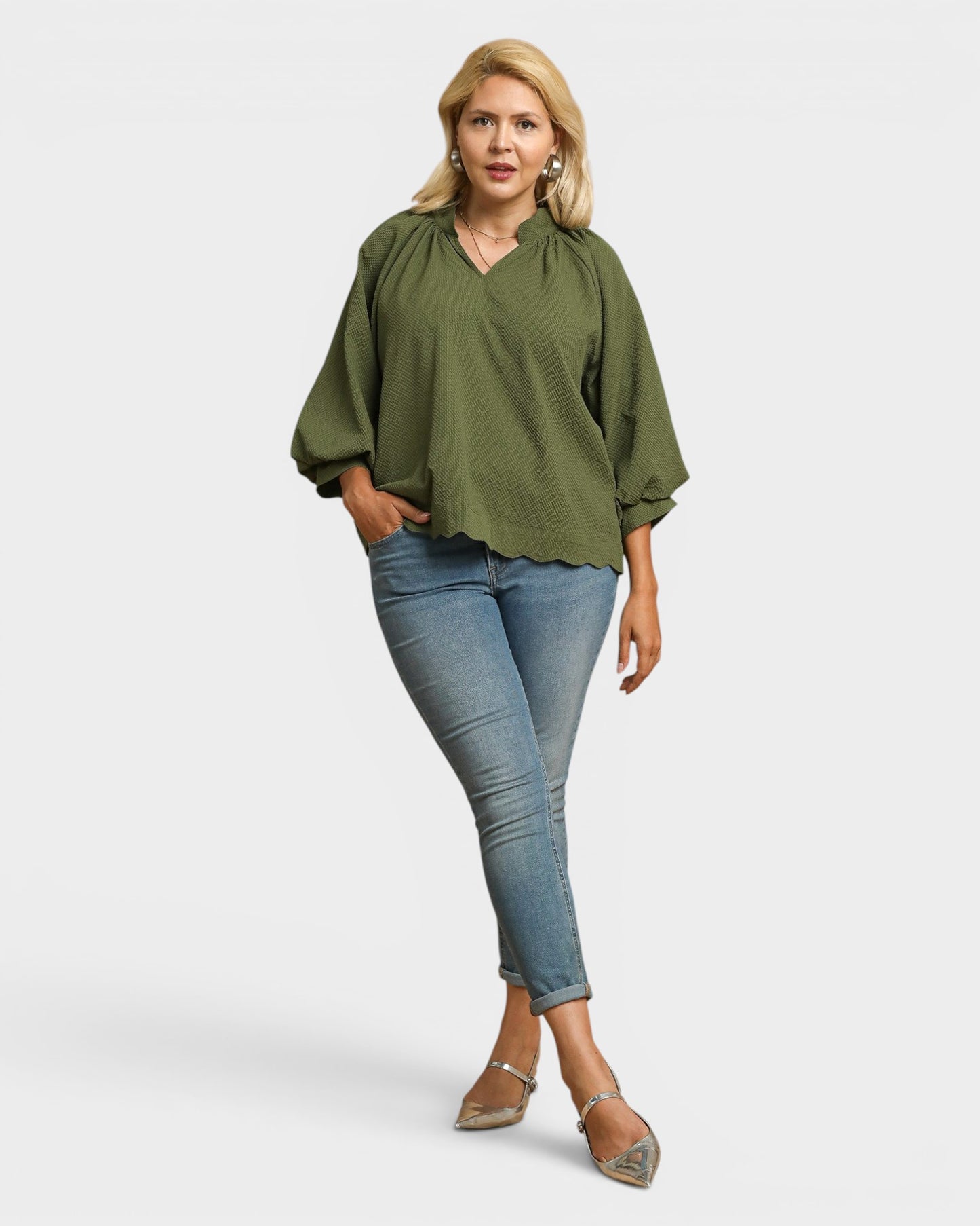 Woman wearing an olive green blouse and blue jeans on a white background