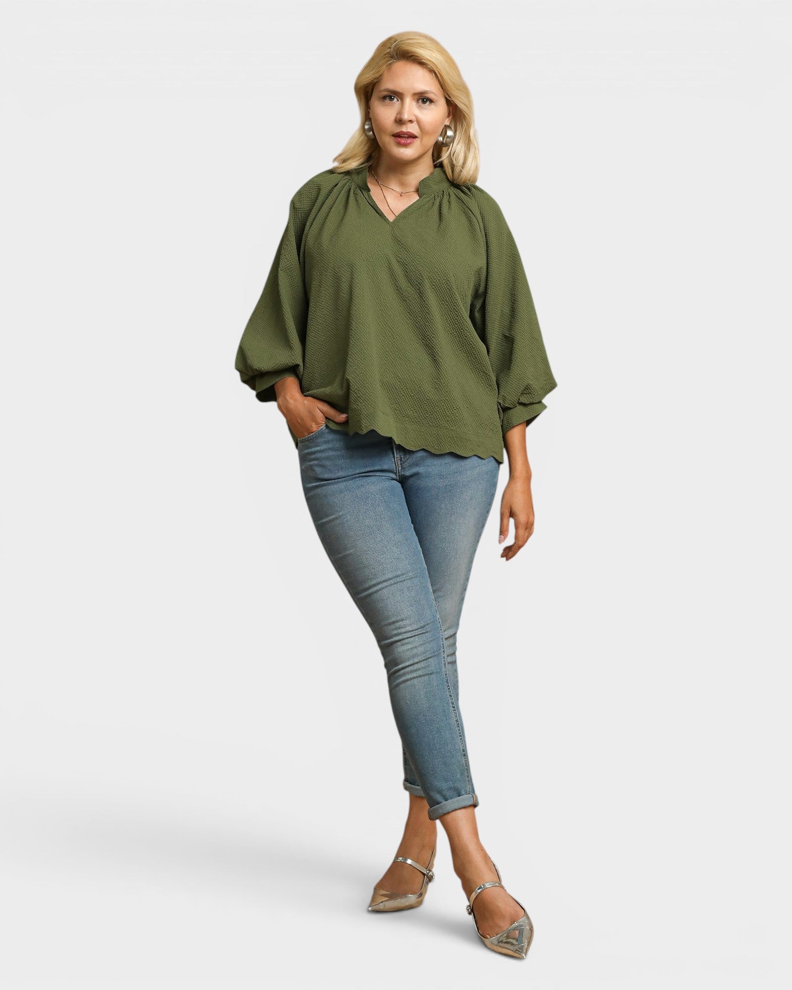 Woman wearing an olive green blouse and blue jeans on a white background