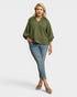 Woman wearing an olive green blouse and blue jeans on a white background