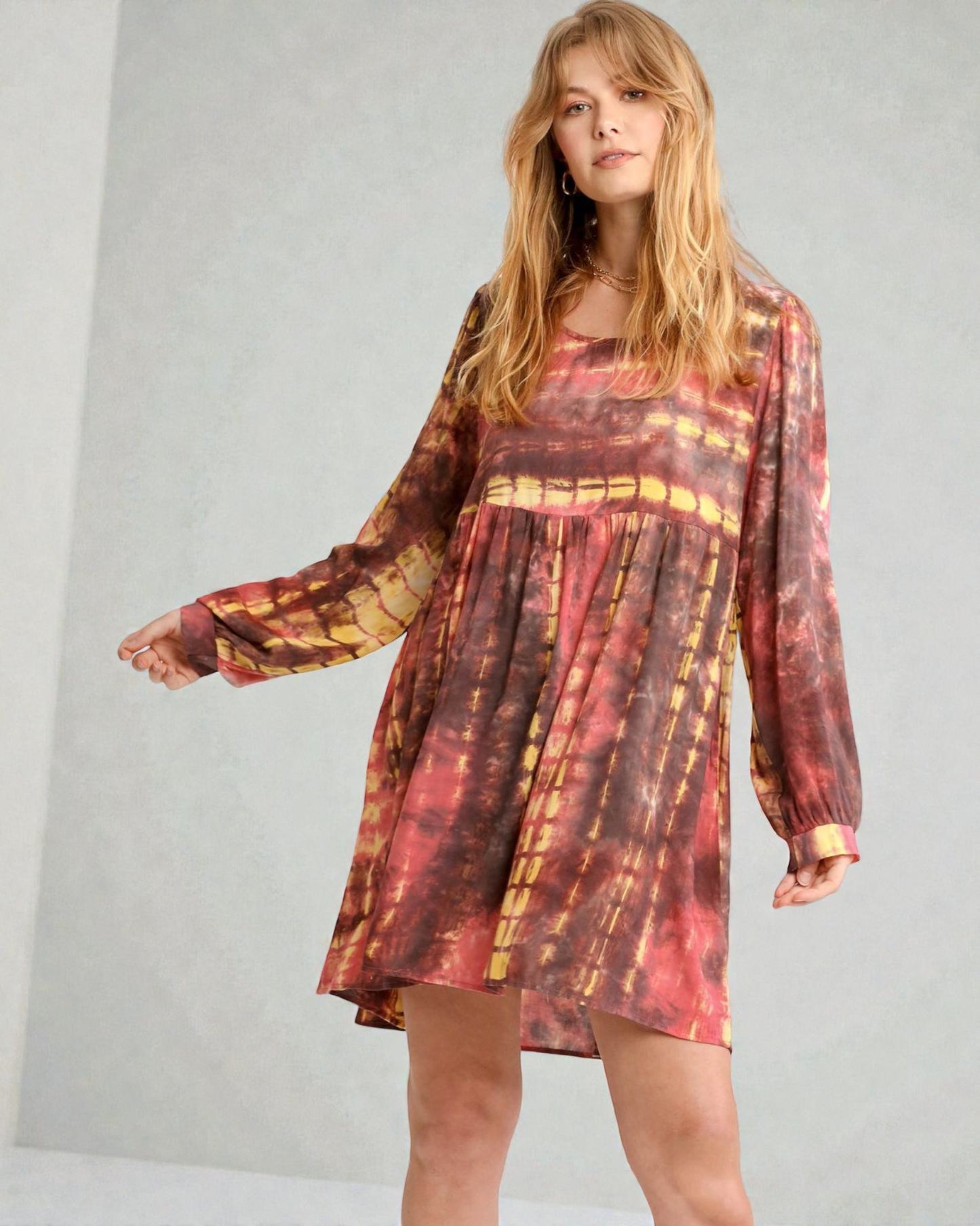 Woman wearing a tie-dye dress with long sleeves on a plain background