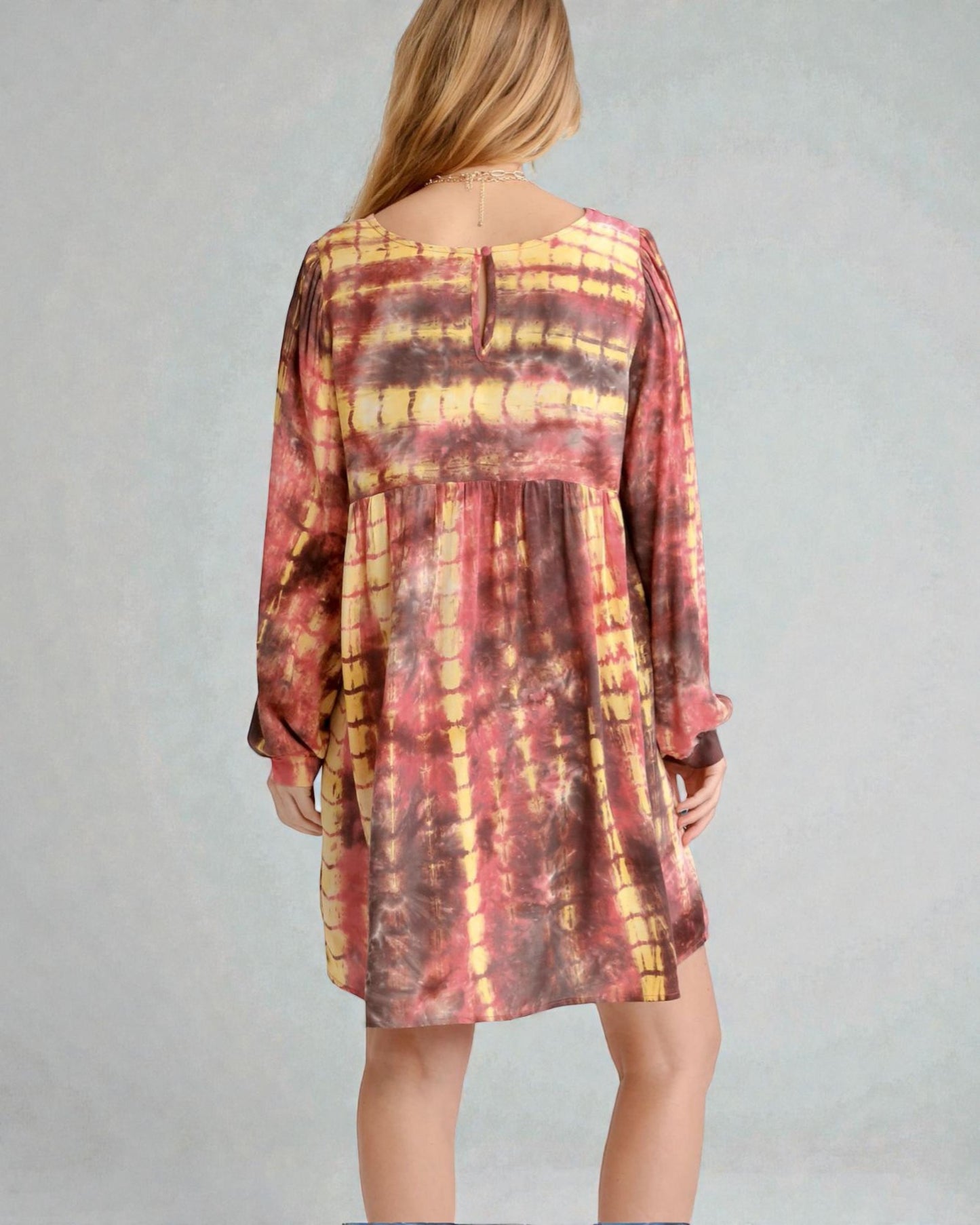 Person wearing a tie-dye dress with long sleeves on a plain background