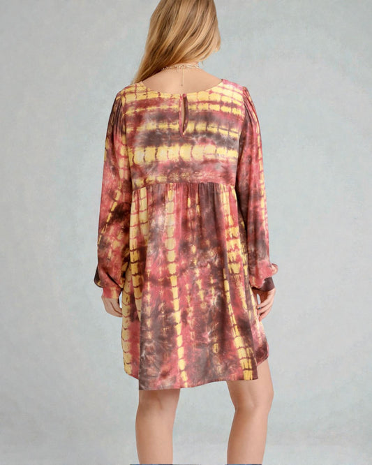 Person wearing a tie-dye dress with long sleeves on a plain background