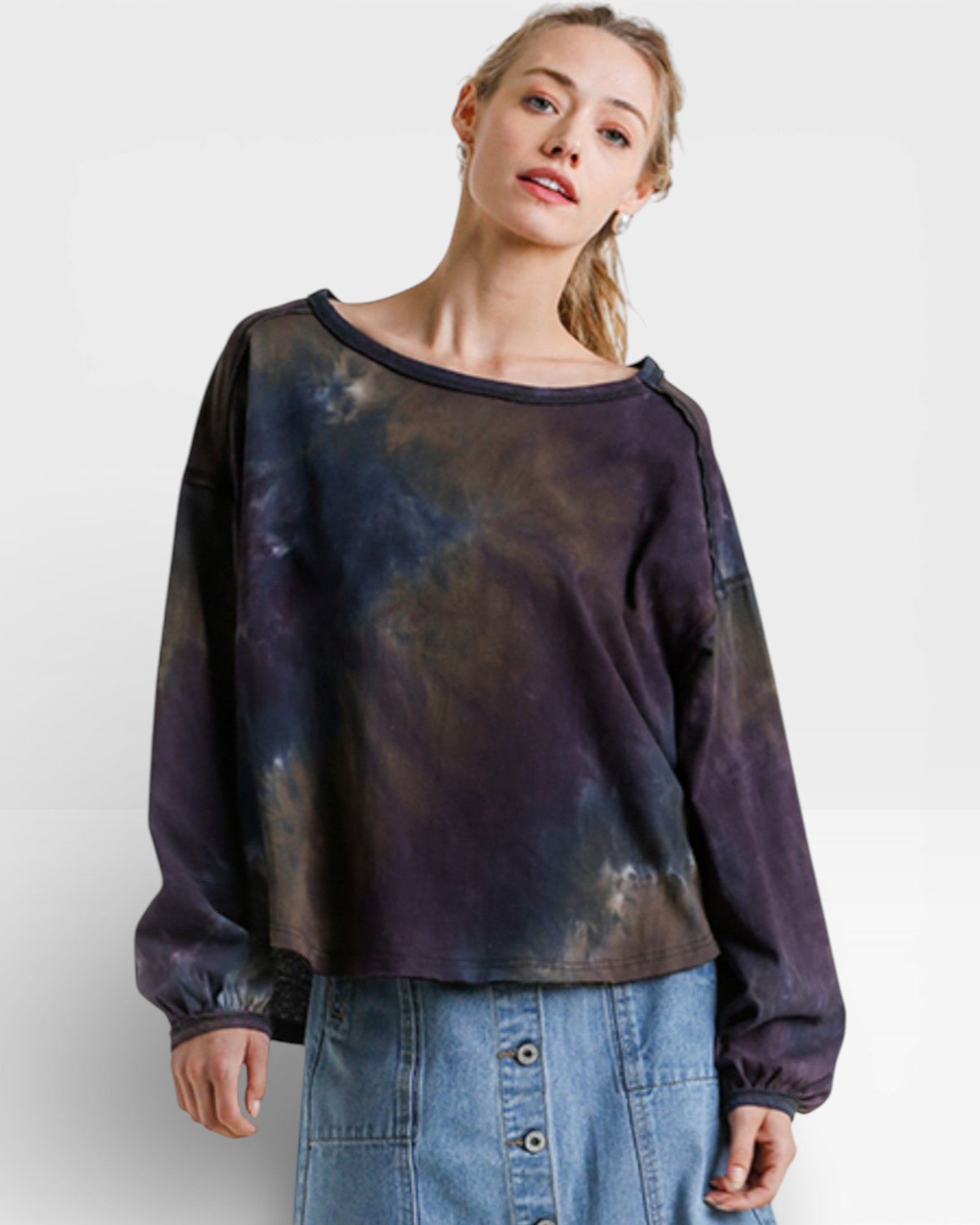 Woman wearing a tie-dye long-sleeve shirt and denim skirt on a white background