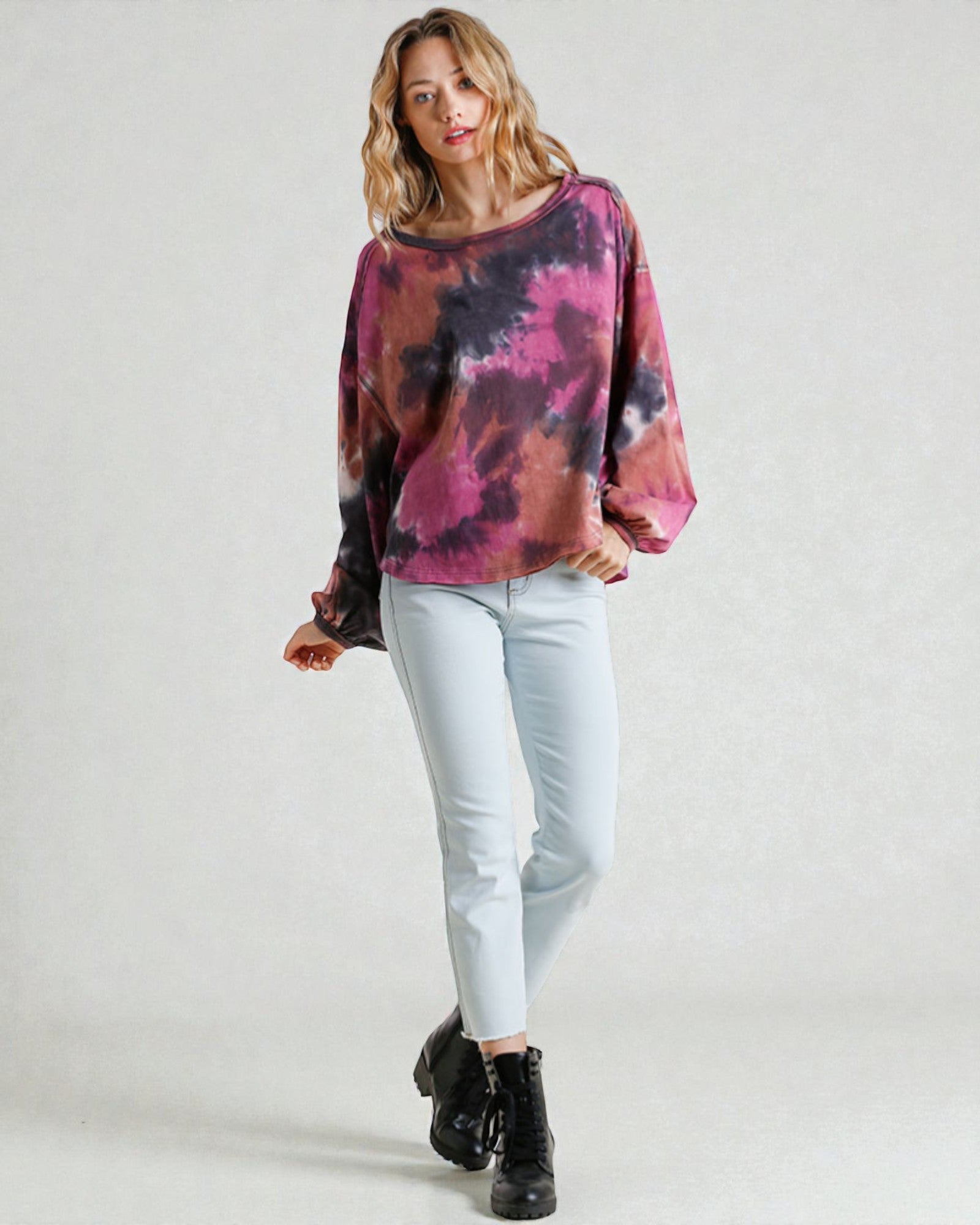 Woman wearing a tie-dye shirt and light blue jeans on a white background