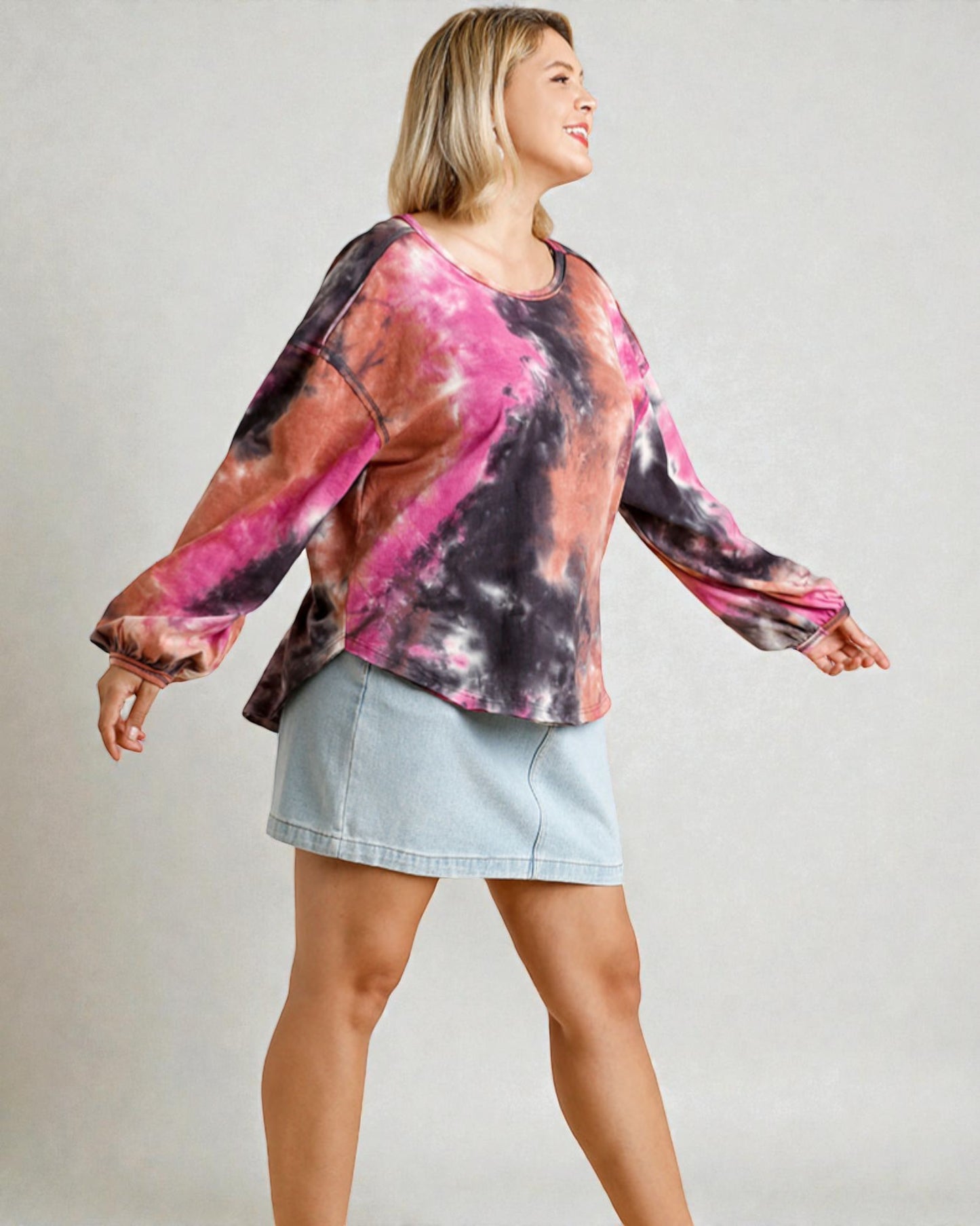 Woman wearing a tie-dye long-sleeve shirt and denim skirt on a plain background