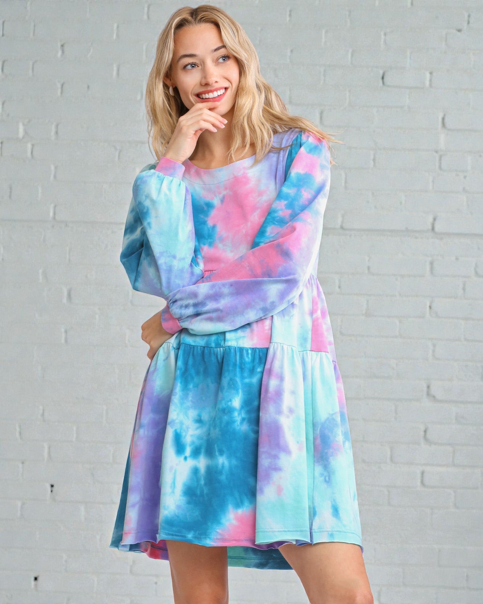 Woman wearing a tie-dye dress against a white brick wall